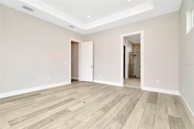 unfurnished bedroom with light wood-type flooring, a tray ceiling, and ensuite bath