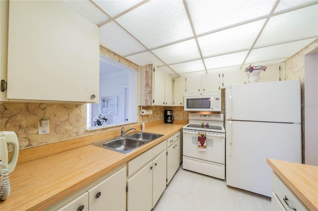 kitchen with white appliances, a paneled ceiling, sink, and light tile floors