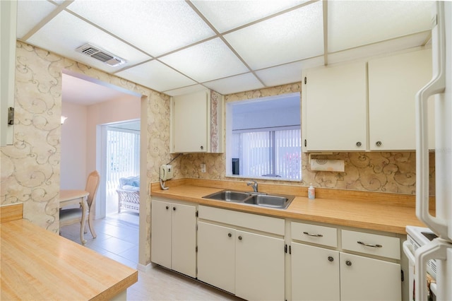 kitchen with white cabinetry, backsplash, light tile flooring, sink, and a paneled ceiling