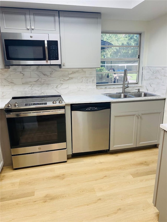 kitchen featuring appliances with stainless steel finishes, gray cabinetry, light hardwood / wood-style floors, and sink