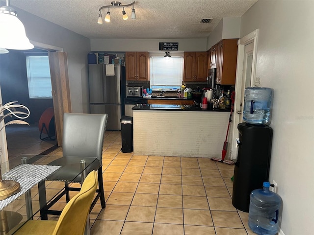 kitchen with a textured ceiling, light tile floors, and stainless steel fridge