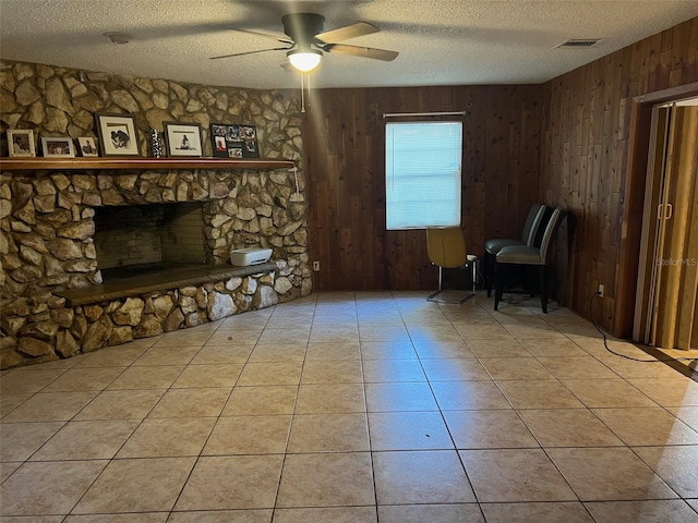 interior space featuring a fireplace, wood walls, light tile flooring, and ceiling fan