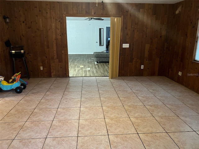 unfurnished room featuring wooden walls, ceiling fan, and light tile floors