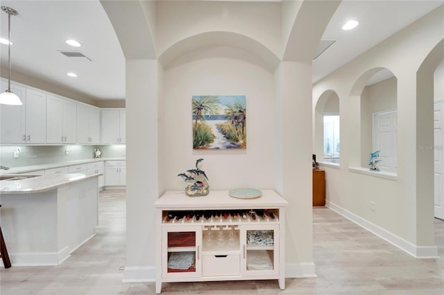 kitchen with hanging light fixtures, white cabinetry, light hardwood / wood-style flooring, light stone counters, and tasteful backsplash