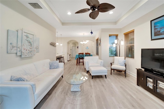 living room with ceiling fan with notable chandelier, a raised ceiling, and light wood-type flooring