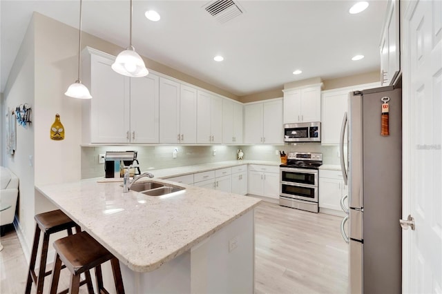 kitchen with sink, appliances with stainless steel finishes, backsplash, a breakfast bar area, and light hardwood / wood-style floors