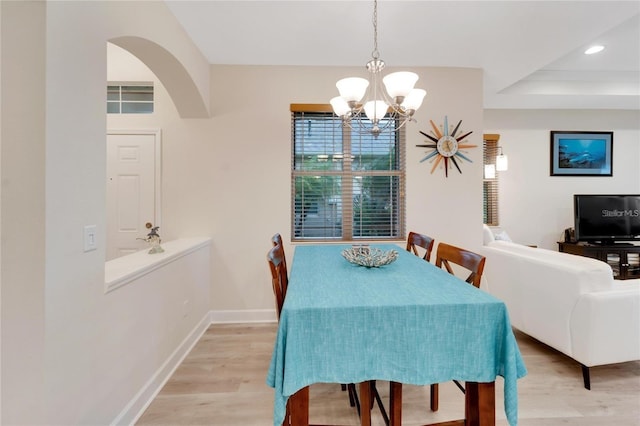 dining space featuring a raised ceiling, light wood-type flooring, and an inviting chandelier