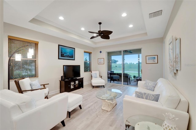 living room with a water view, light hardwood / wood-style floors, ceiling fan, and a tray ceiling