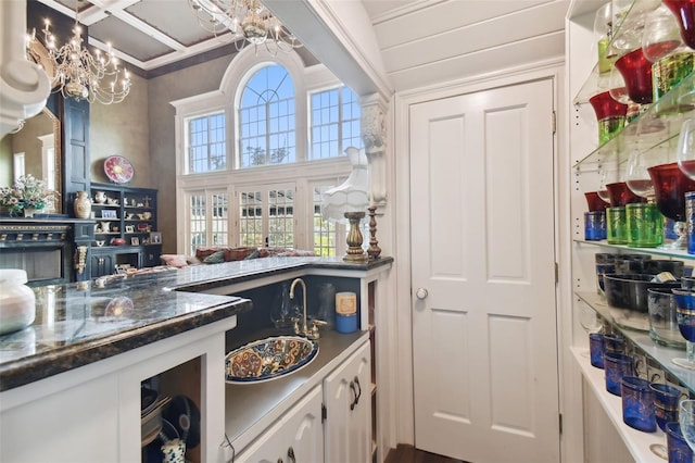 bar with white cabinetry, dark stone counters, coffered ceiling, and a notable chandelier