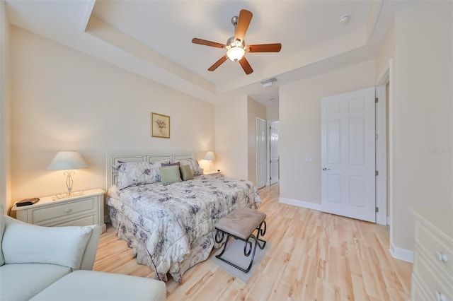 bedroom featuring ceiling fan, a raised ceiling, and light wood-type flooring