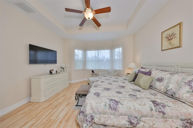 bedroom with ceiling fan, light hardwood / wood-style flooring, and a raised ceiling