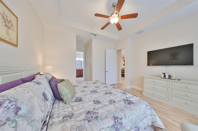 bedroom featuring ceiling fan, connected bathroom, a tray ceiling, and light wood-type flooring