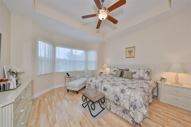 bedroom with ceiling fan, multiple windows, light hardwood / wood-style flooring, and a tray ceiling