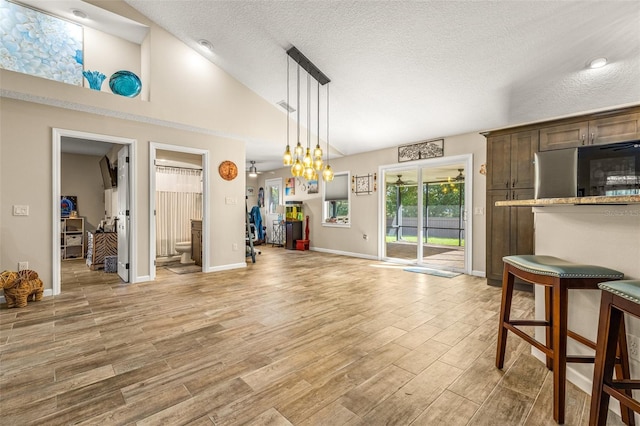 interior space featuring light wood-type flooring, high vaulted ceiling, a notable chandelier, and a textured ceiling