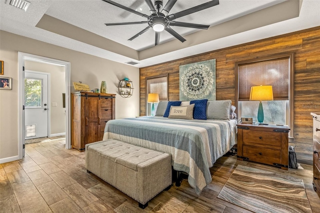 bedroom featuring hardwood / wood-style flooring, ceiling fan, a textured ceiling, wooden walls, and a tray ceiling