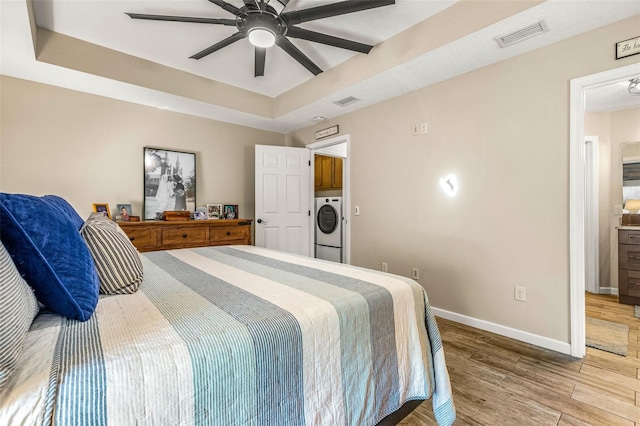 bedroom featuring washer / clothes dryer, hardwood / wood-style floors, a raised ceiling, and ceiling fan