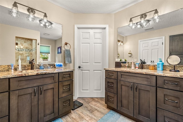 bathroom with a textured ceiling, hardwood / wood-style flooring, and dual bowl vanity