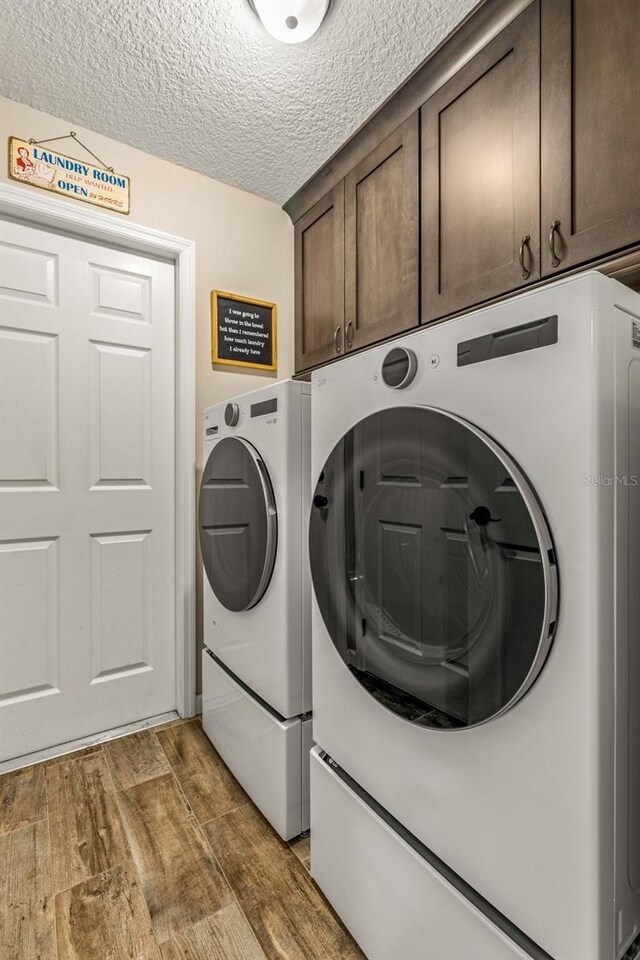 clothes washing area with hardwood / wood-style floors, cabinets, a textured ceiling, and washing machine and dryer