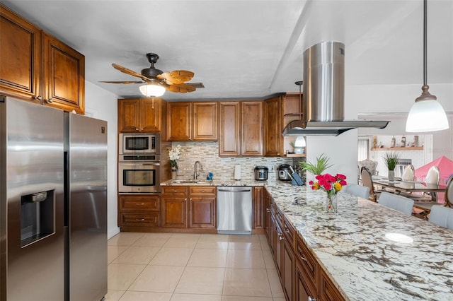 kitchen with appliances with stainless steel finishes, hanging light fixtures, light stone countertops, island exhaust hood, and sink