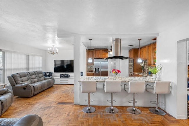 kitchen featuring a breakfast bar, kitchen peninsula, island range hood, stainless steel appliances, and a chandelier