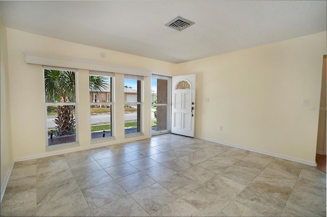 empty room with visible vents, a textured ceiling, and baseboards