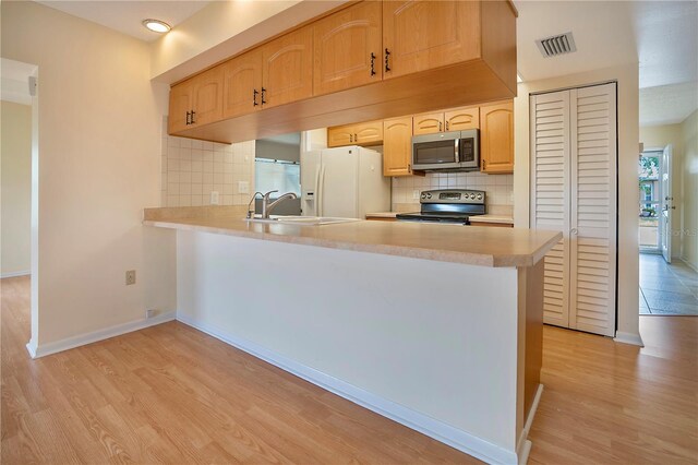 kitchen with backsplash, kitchen peninsula, stainless steel appliances, and light wood-type flooring