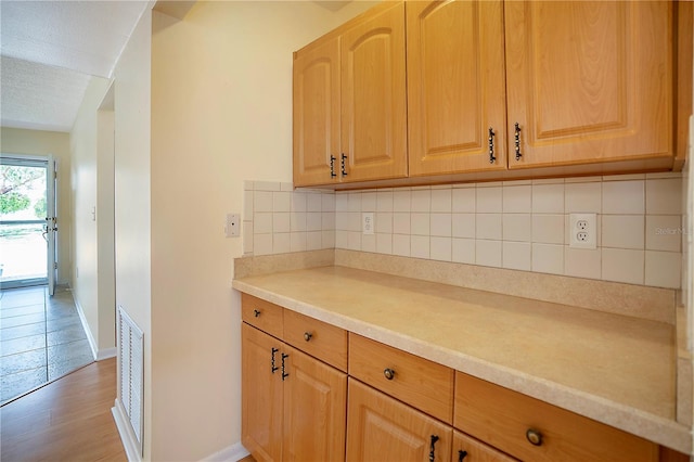 kitchen featuring light wood finished floors, visible vents, baseboards, light countertops, and decorative backsplash