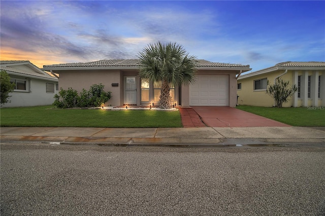 view of front of house with stucco siding, driveway, a tile roof, a front yard, and a garage