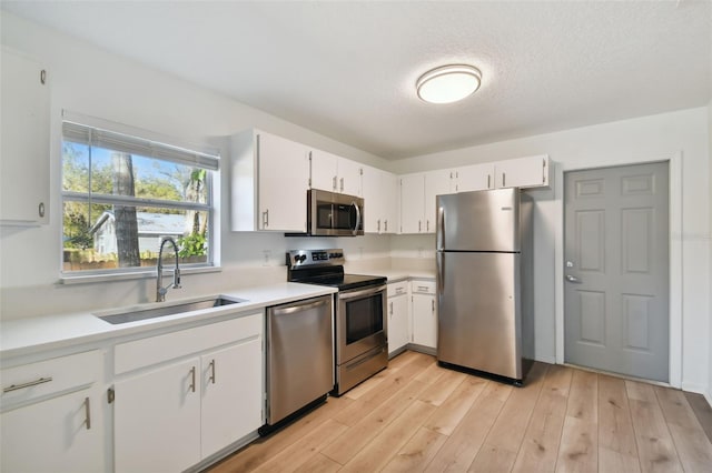 kitchen with appliances with stainless steel finishes, light hardwood / wood-style floors, white cabinetry, and sink