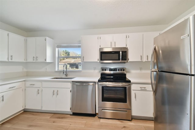 kitchen with sink, stainless steel appliances, light wood-type flooring, and white cabinetry