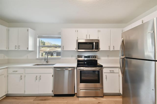 kitchen featuring appliances with stainless steel finishes, white cabinetry, sink, and light wood-type flooring