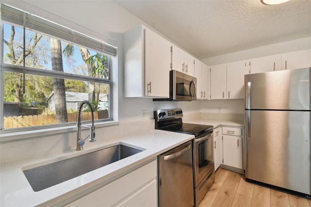 kitchen with white cabinets, sink, stainless steel appliances, and light hardwood / wood-style floors