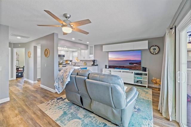 living room featuring ceiling fan, a textured ceiling, and light hardwood / wood-style flooring