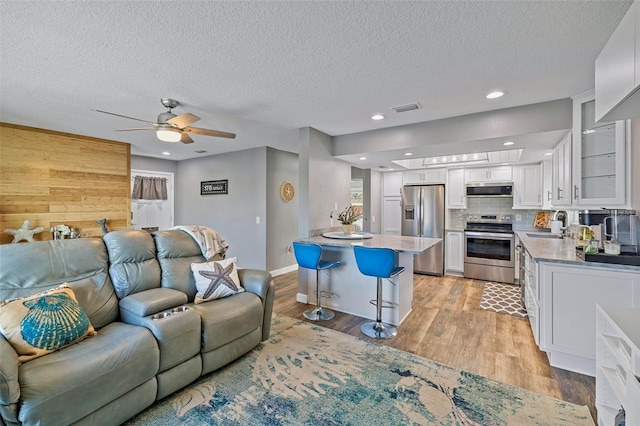 living room with light wood-type flooring, a textured ceiling, ceiling fan, wooden walls, and sink