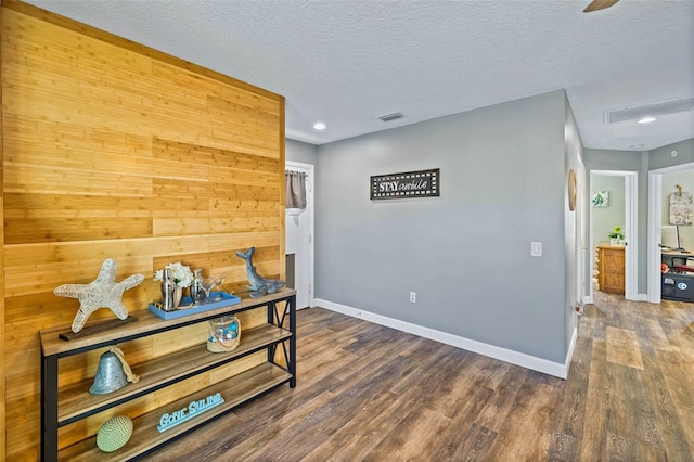 corridor featuring a textured ceiling, dark wood-type flooring, and wood walls