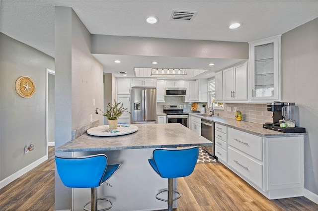 kitchen featuring white cabinetry, sink, stainless steel appliances, a kitchen breakfast bar, and light wood-type flooring