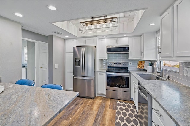 kitchen with sink, decorative backsplash, light wood-type flooring, appliances with stainless steel finishes, and white cabinetry