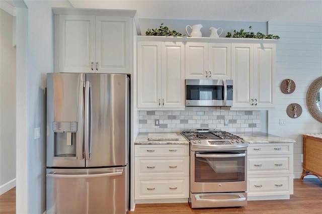 kitchen featuring stainless steel appliances, light stone counters, white cabinetry, and light hardwood / wood-style floors