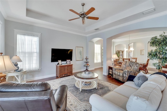 living room with a raised ceiling, ceiling fan with notable chandelier, a wealth of natural light, and wood-type flooring