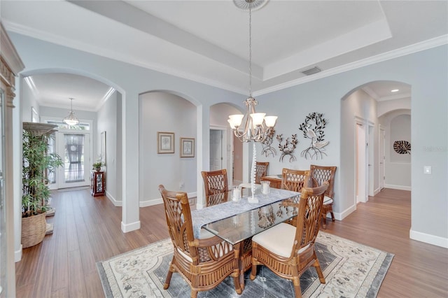 dining space with ornamental molding, hardwood / wood-style floors, an inviting chandelier, and a raised ceiling