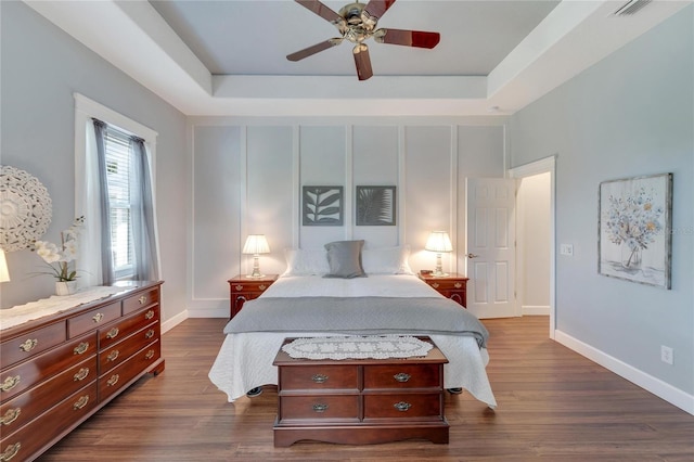 bedroom with a tray ceiling, dark wood-type flooring, and ceiling fan