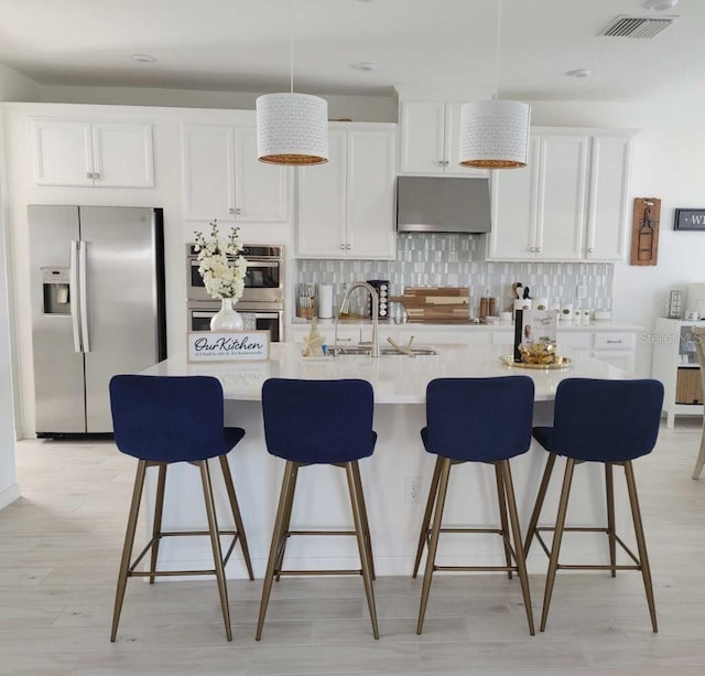 kitchen with backsplash, a center island with sink, stainless steel appliances, and white cabinets