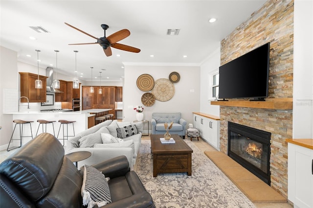 living room featuring ceiling fan, a stone fireplace, and crown molding