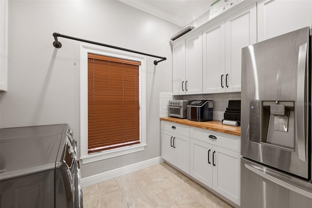 kitchen with decorative backsplash, stainless steel fridge, washing machine and dryer, white cabinetry, and butcher block counters