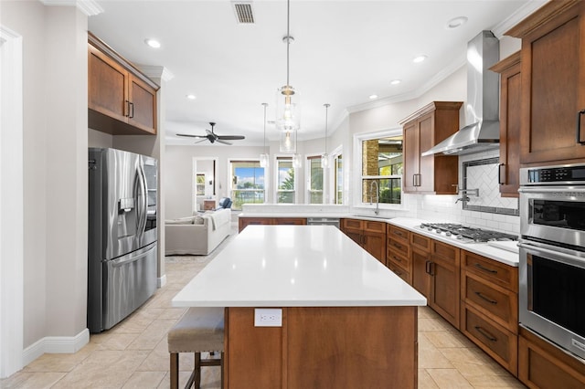 kitchen featuring a center island, wall chimney range hood, sink, appliances with stainless steel finishes, and decorative light fixtures