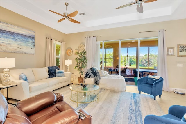 living room with light tile floors, ceiling fan, and a tray ceiling