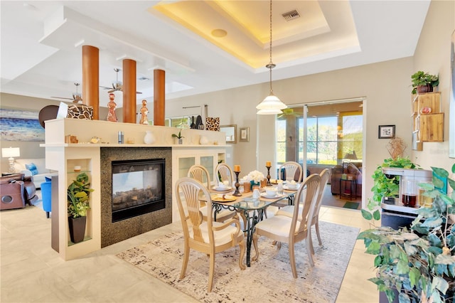 dining space with a raised ceiling, light tile floors, and a multi sided fireplace