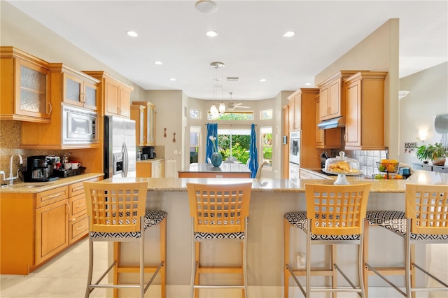 kitchen featuring a chandelier, stainless steel appliances, decorative light fixtures, backsplash, and light stone counters