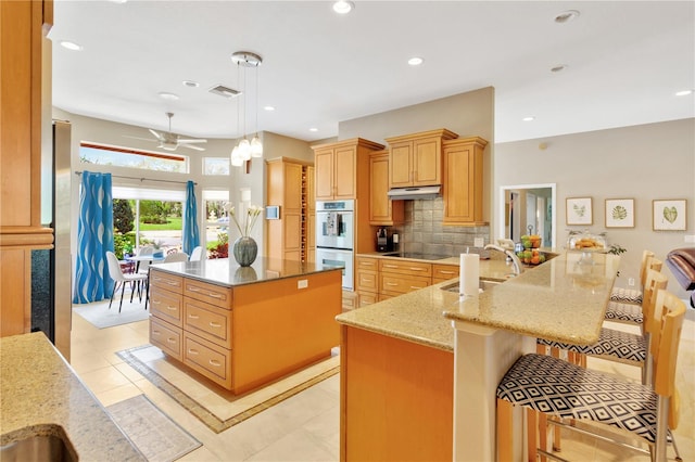 kitchen featuring backsplash, ceiling fan, light stone counters, a kitchen island, and pendant lighting