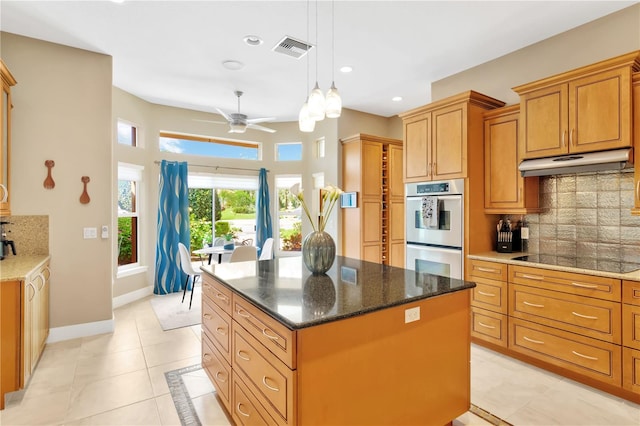 kitchen with double oven, light tile floors, a kitchen island, ceiling fan, and backsplash